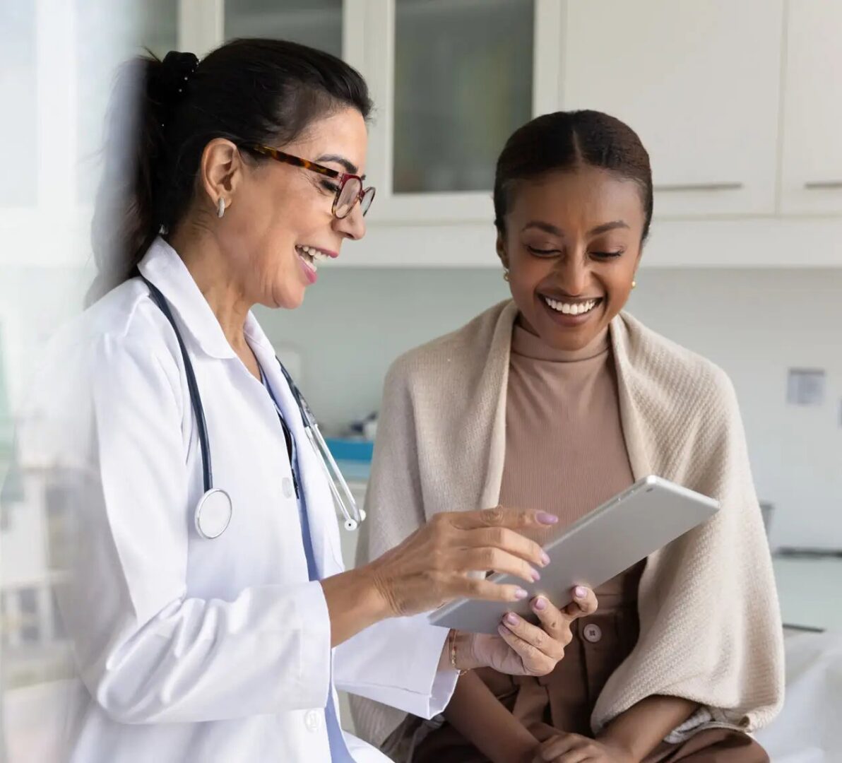 3925d2e3-3381-4f61-90fe-fd60f298546a Happy senior practitioner woman and cheerful young African patient woman watching examination medical report on tablet computer, using digital technology, laughing